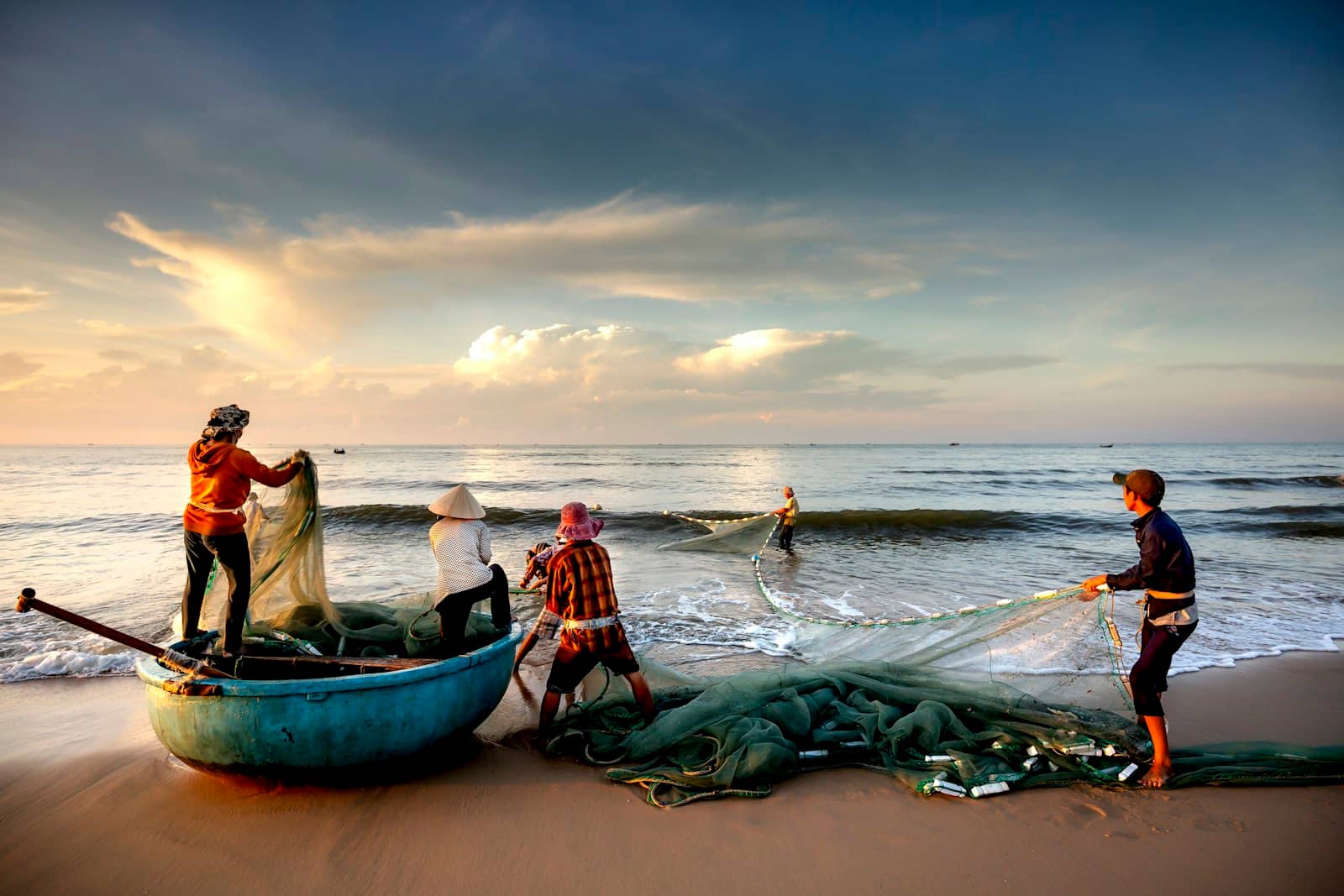 Ngư dân kéo lưới lên bãi cát lúc bình minh, bên cạnh chiếc thuyền thúng xanh
