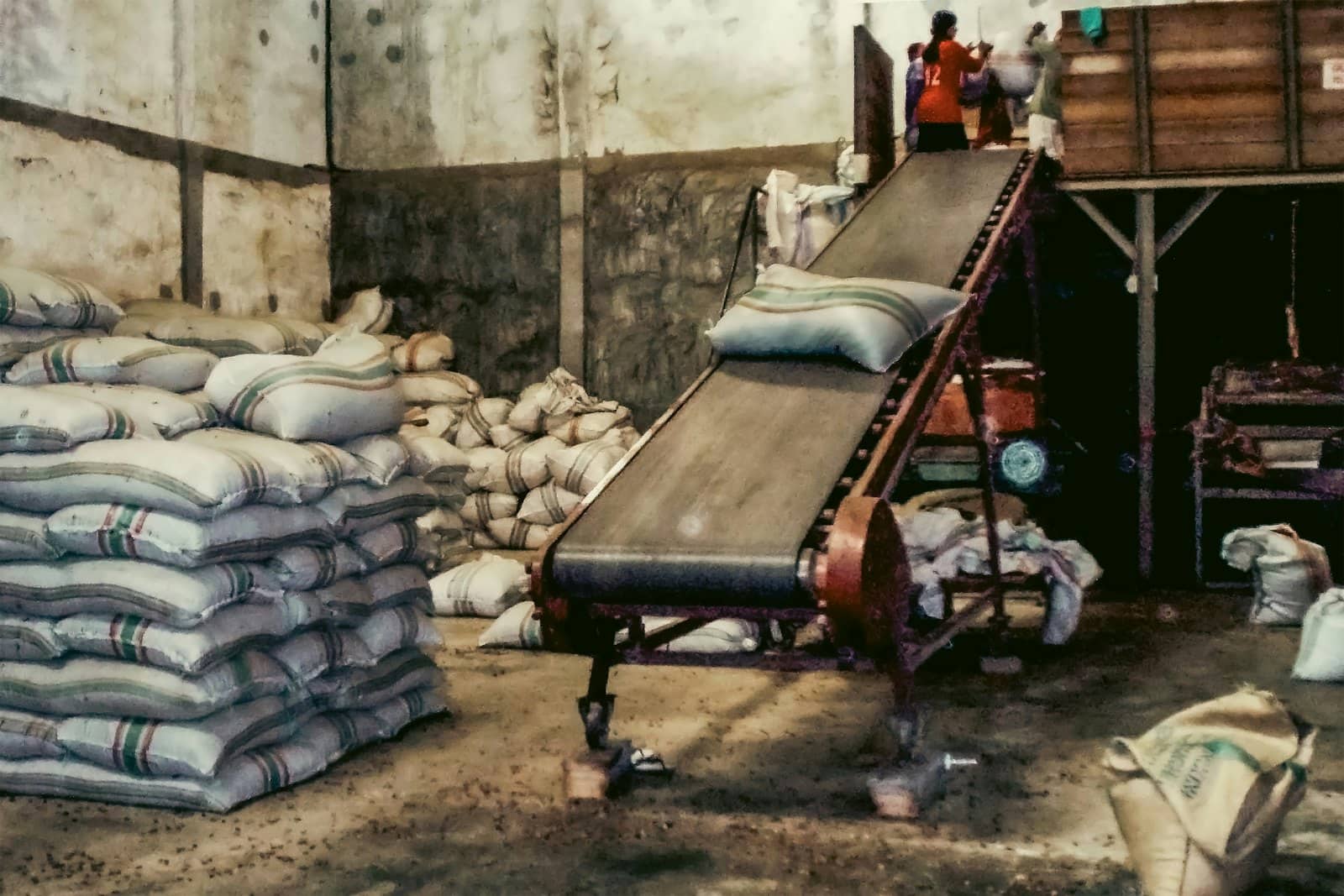 Băng chuyền đưa bao hàng lên sàn trong kho, bên cạnh những chồng bao tải xếp cao